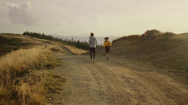 Wide shot female and male athletes running on road in mountains Sporty couple doing cardio workout outdoor Active woman and man looking around summer landscape