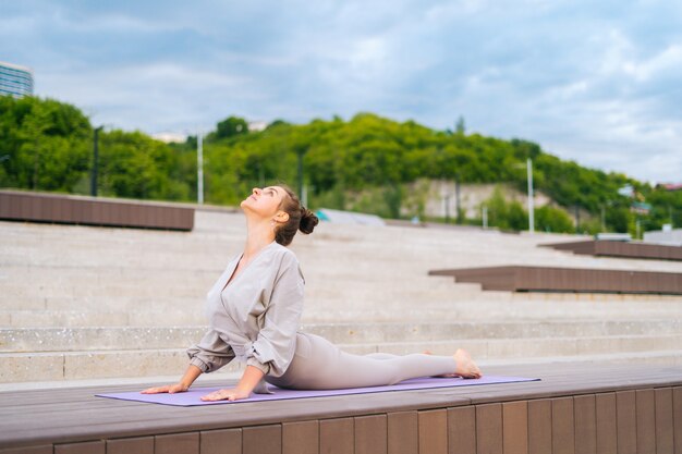 Wide shot of flexible young yogini woman practicing yoga exercisers on fitness mat on summer day