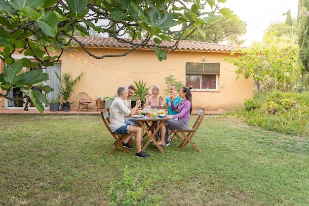 Foto immagine ampia di amici che mangiano e bevono nel patio persone di mezza età allegre attorno al tavolo