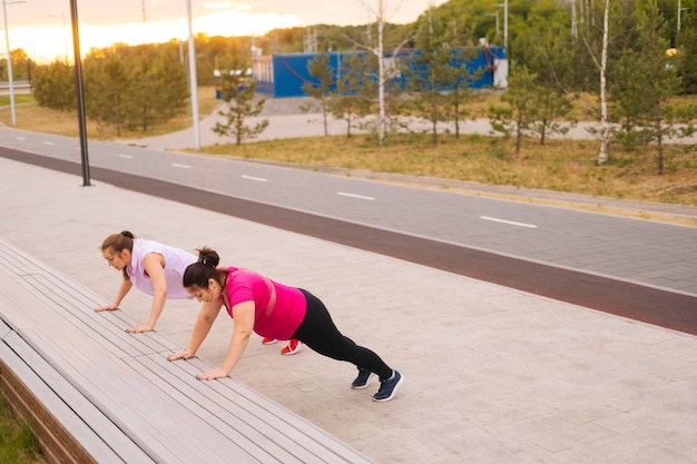 Общий снимок персональной тренировки спортивной дамы для тучной женщины с большим животом на открытом воздухе