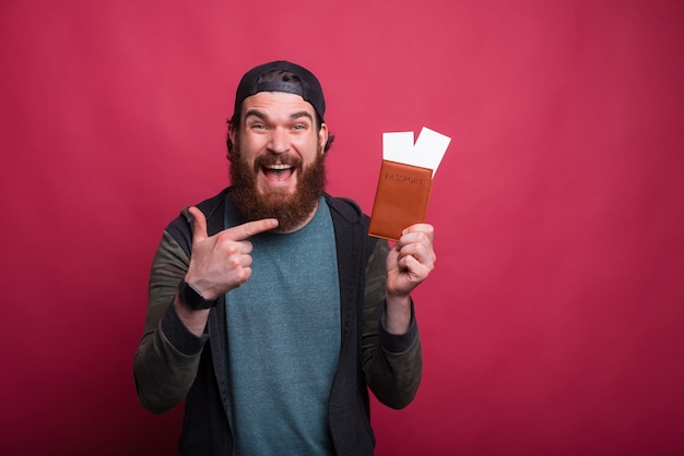 Wide smiling man is pointing at his passport with tickets