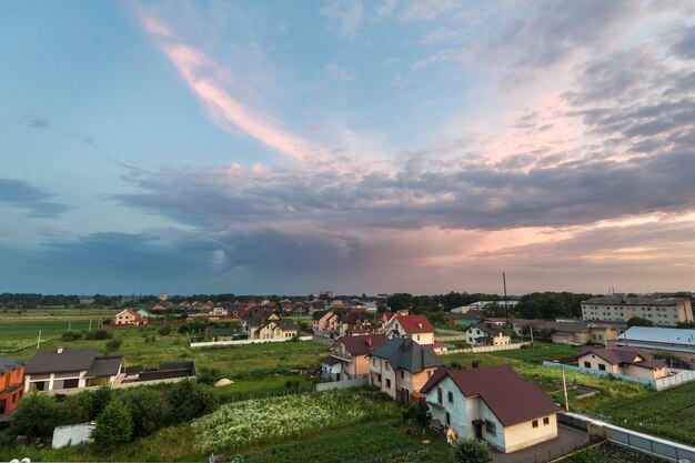 Wide summer panorama of new quiet residential suburban area. Land plots and new modern houses among green trees under cloudy sky at sunset. Construction, selling and investment in real estate concept.