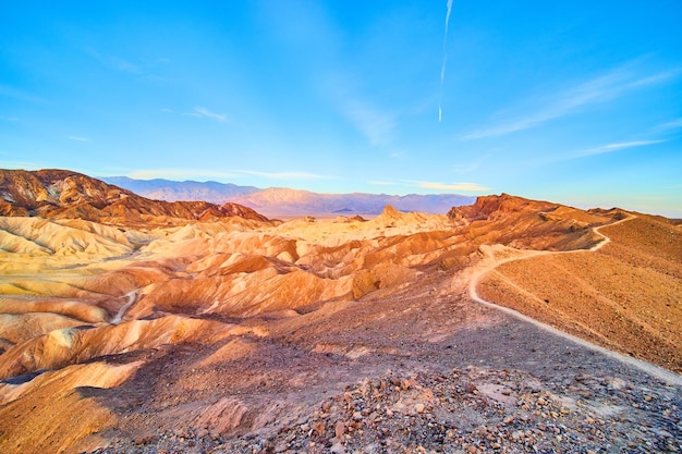 Wide view of hiking path along top of mountains at Death Valley with colorful sunrise waves