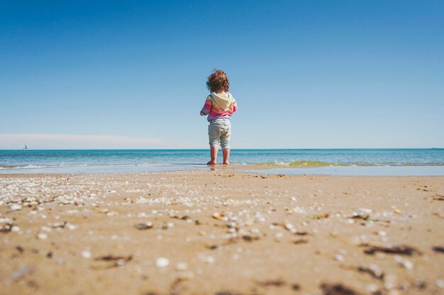 Wide view of a little girl wearing rainbow hoodie playing at the beach                          barefoot