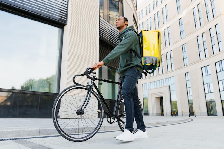 Photo a wideangle shot from below of an africanamerican pizza deliveryman next to a bicycle against the background of modern buildings