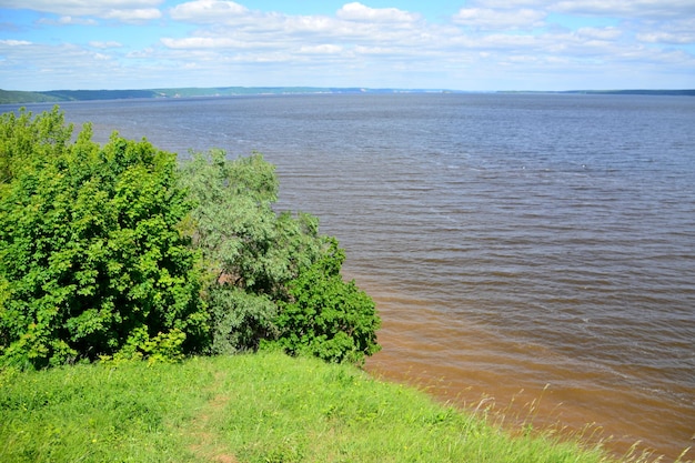 The widest place of volga river with blue sky and clouds on horizon, view from green hill and tree