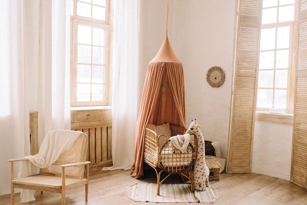 Wieg met een cape in een lichte slaapkamer met grote ramen speelgoedgiraf en loungefauteuil