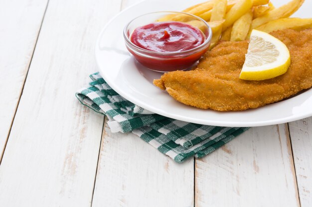 Wiener schnitzel with fried potatoes on white wooden