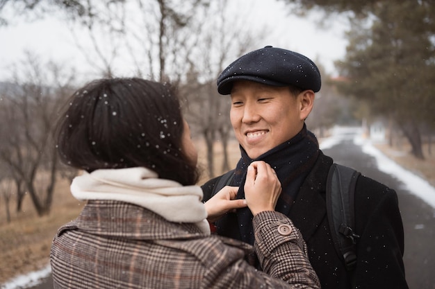 Wife adjusts scarf of husband at romantic walk in park in winter