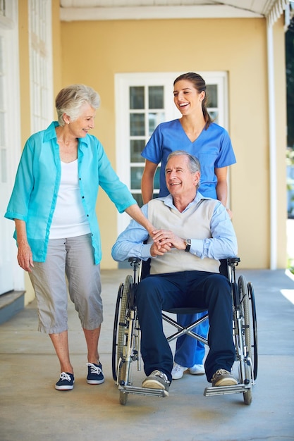 Wife caregiver laughing or old man in wheelchair in hospital clinic helping an elderly patient for support Funny happy or healthcare nurse speaking or smiling with senior people with a disability