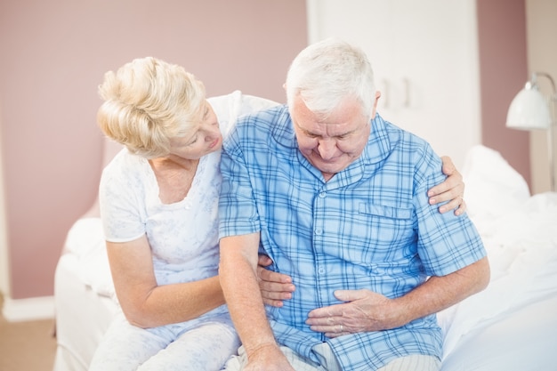 Wife comforting senior husband suffering from stomach pain