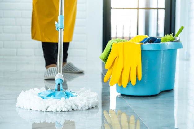 Photo wife housekeeping and cleaning concept, happy young woman in blue rubber gloves wiping dust using mop while cleaning on floor at home
