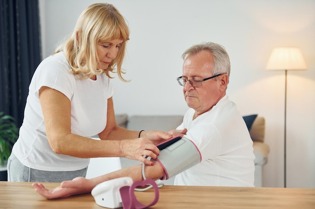 Wife measuring blood preasure of her husband Senior man and woman is together at home