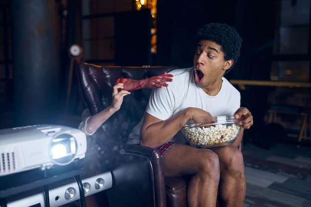 Wife scares husband with bloody hand from behind chair during home film watching on projector