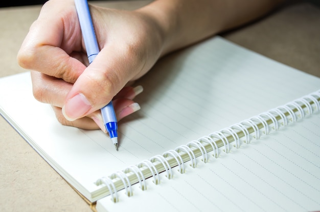 Wijfje dat een blauwe pen houdt schrijvend op notitieboekje op houten lijst