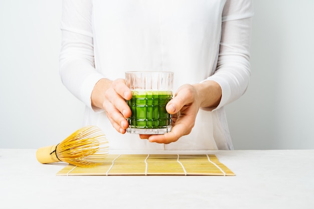 Wijfje in witte kleren die het glas met Japanse Matcha-thee of groene smoothie houden