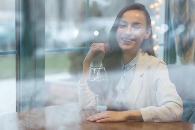 Wijn drinken. vrolijke mooie onweerstaanbare vrouw die met haar speelt terwijl ze naar de camera staart en een glas wijn aanraakt