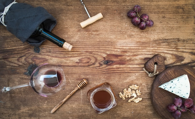 Wijn en voorgerecht ingesteld met kopie ruimte in het midden. Glas rode wijn, fles, kurkentrekker, blauwe kaas op portie bord, druiven, honing, walnoten over rustieke houten tafel, bovenaanzicht.