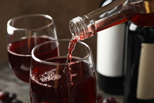 Wijn wordt gegoten uit een fles in glas op houten tafel, close-up