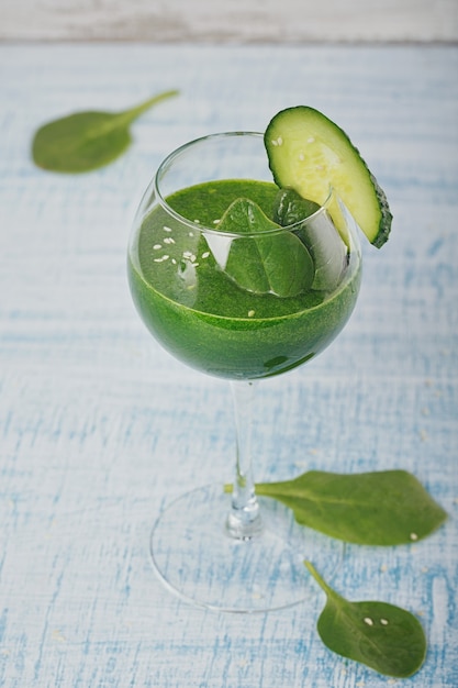 Wijnglas gevuld met verse groene spinazie en komkommer smoothie op lichtblauwe houten ondergrond. Niet-alcoholische dranken. Gezond eten en vegetarisch concept.
