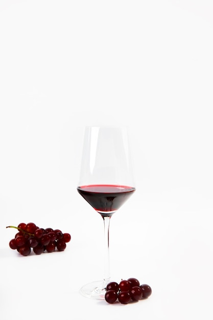 Wijnglas met een scheutje rode wijn en druiven geïsoleerd op een witte achtergrond kopie ruimte