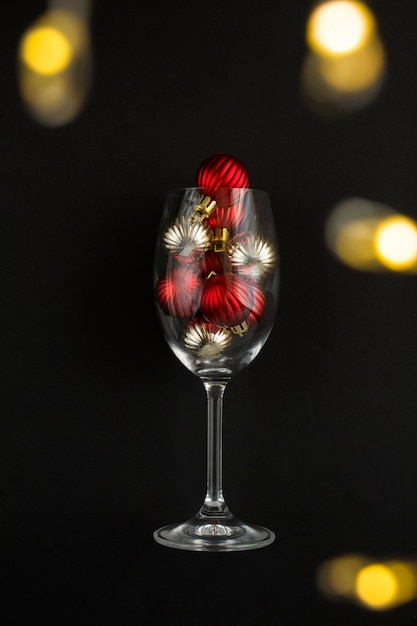 Wijnglas met rode en gouden kerstballen op de zwarte achtergrond. detailopname. locatie verticaal.