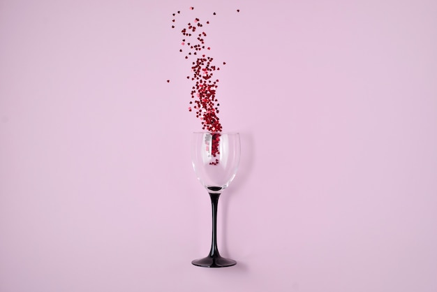 Wijnglas uitgegoten rode hart confetti op roze kleur papier achtergrond.