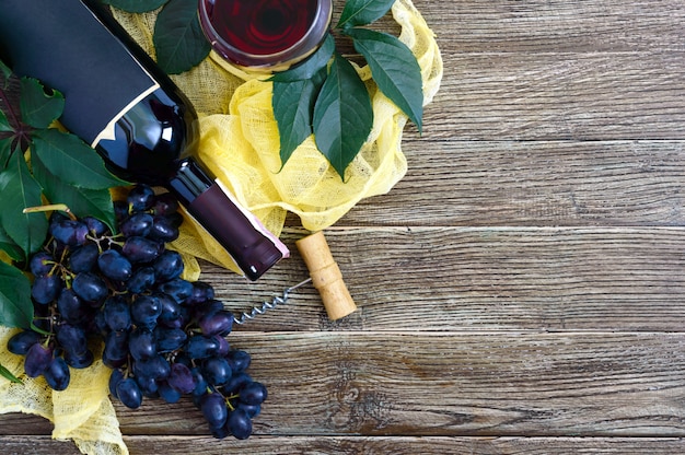 Wijnglazen met rode wijn, fles, kurkentrekker, blauwe druiven, bladeren op een houten tafel.