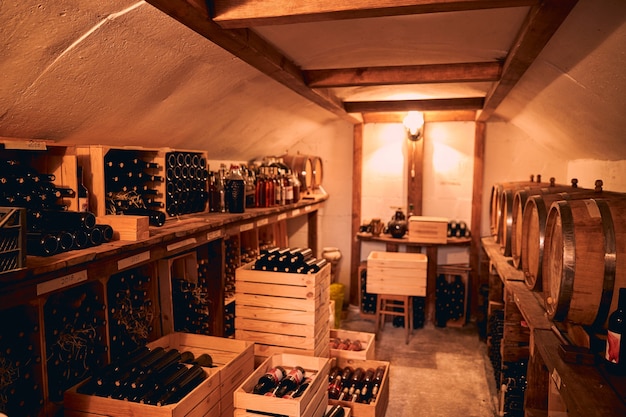 Foto wijnkelder met flessen alcoholische drank in houten kisten en vaten op houten stands
