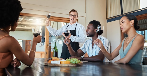 Wijnproevende vrienden en wijn in een restaurant of wijngaard leren over de groei en productie van druiven Groep met een wijnglas in de hand luisterend naar de ober die praat over een rode wijnmelange voordat ze drinken