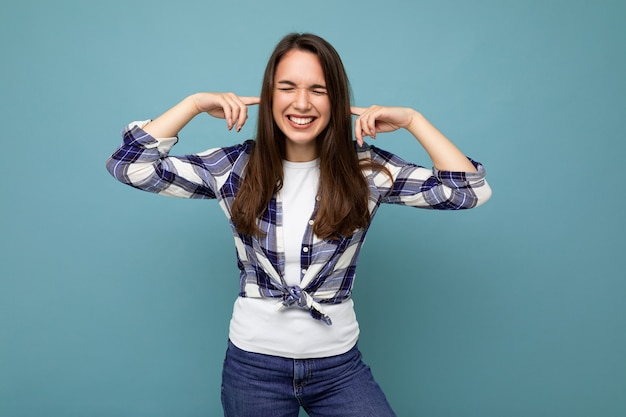 Wil het niet horen. Jonge emotionele positieve en glimlachende aantrekkelijke donkerbruine vrouw die geruit overhemd draagt