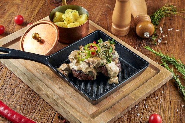 Wild boar cutlets with boiled potatoes and creamy sauce with wild mushrooms on a wooden surface in composition with spices on a wooden surface