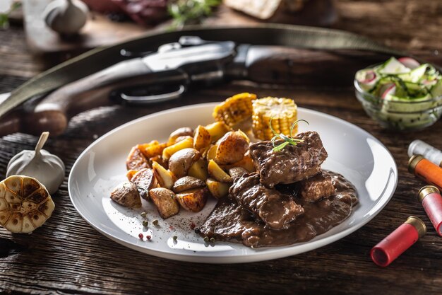 Lo stufato di goulash di selvaggina selvaggia servito con patate arrostite e condito con peperoncino a quattro colori l'intero cibo è circondato da fucili da caccia e proiettili di pistola