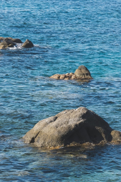 野生の岩の多いビーチの海岸線と海の波が海岸の岩に飛び散る穏やかな海白い海の泡を作成する海岸の岩に波が砕ける