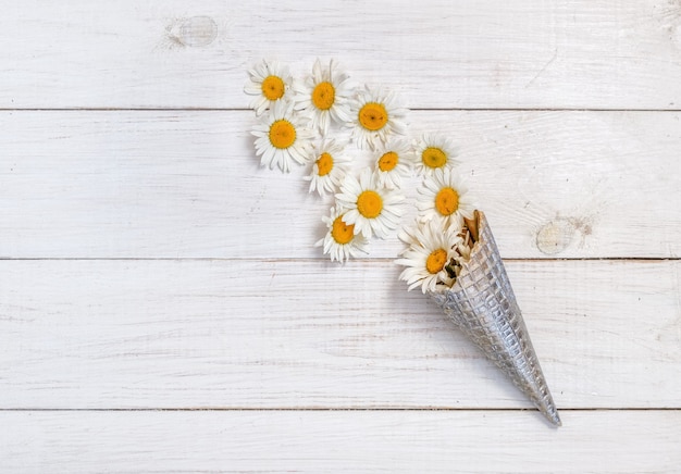 Wild white daisies in a silver waffle horn on a white wooden table