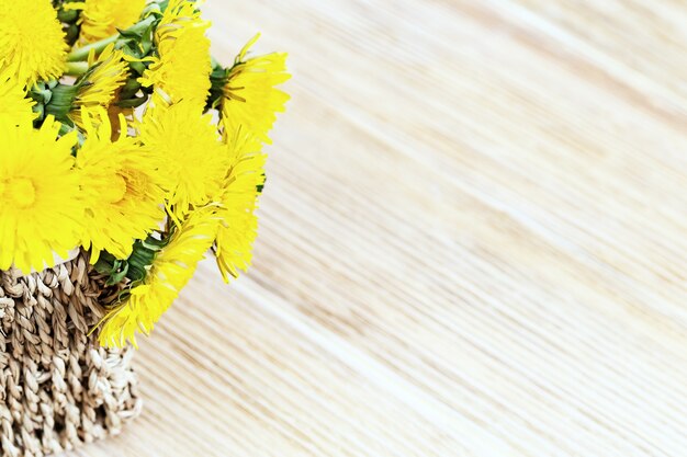 Wilde bloemen blowball, helder gele Lentebloemen in rieten mand op hout. Rustieke stijl met kopie ruimte.