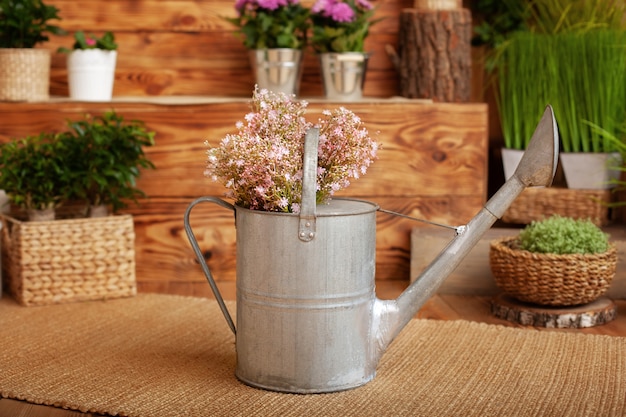 Wilde bloemen in gieters. Tuingereedschap, kamerplanten en bloemen op het terras in de tuin. Concept van tuinieren en hobby. Lente tuin. Boeket zomerbloemen in metalen gieter op veranda.