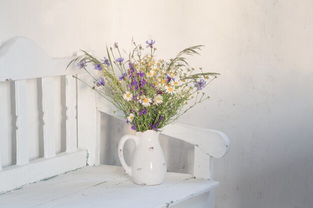 Wilde bloemen in kruik op witte houten bankje