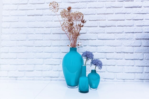 Foto wilde bloemen in turquoise vazen op een witte tafel tegen een witte kerpwand. wilde bloemen in een vaas.