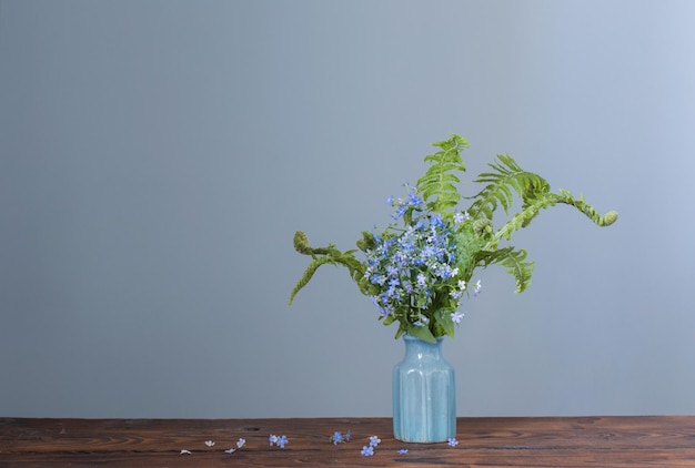 Wilde bloemen in vaas op blauwe achtergrondmuur