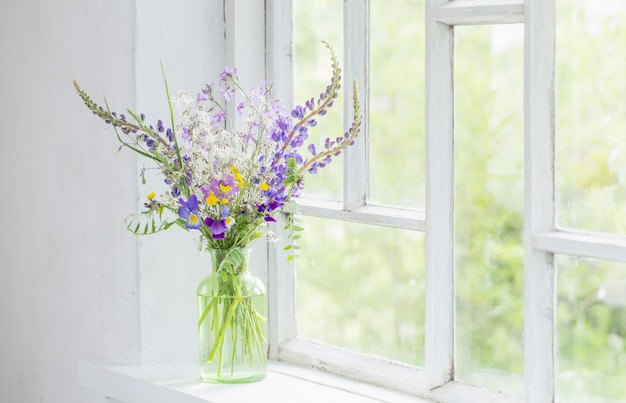 Wilde bloemen in vaas op witte vensterbank