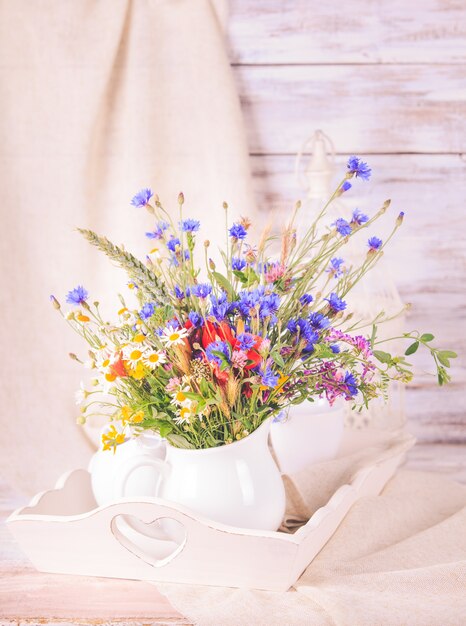 Wilde bloemen in witte keramische kan en kopjes op dienblad