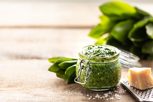 Wilde prei pesto met olijfolie en Parmezaanse kaas in een glazen pot op een houten tafel. Nuttige eigenschappen van ramson. Bladeren van verse ramson. Kopieer ruimte