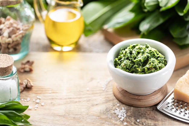 Wilde prei pesto met olijfolie en Parmezaanse kaas in een witte keramische mortel op een houten tafel. Nuttige eigenschappen van ramson. Kopieer ruimte.