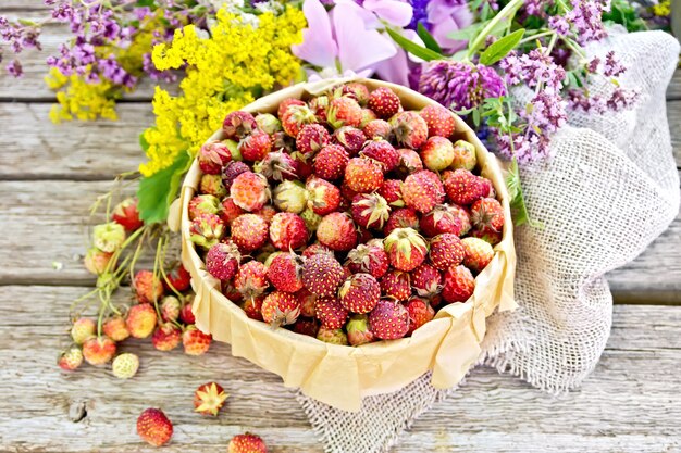 Wilde rijpe aardbeien in een schorsdoos met perkament, jute en wilde bloemen op de achtergrond van oude houten planken