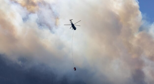 Wildfire Service Helicopter flying over BC Forest Fire and Smoke on the mountain near Hope