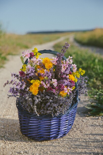 かごの中の野花。フィールドロードのバスケットにさまざまな花の花束。トーン。