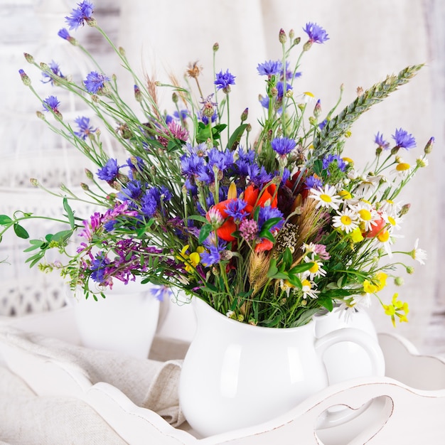 Фото Полевые цветы в белом керамическом кувшине и чашки на подносе