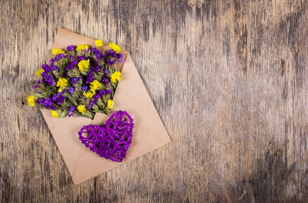 Wildflowers in paper envelope and wicker heart