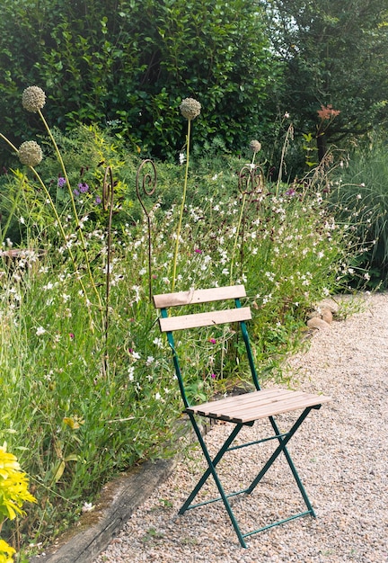 Wildflowers and tall green vegetation in a garden next to an empty wooden and metal chair on stone path Concept of relax and rest in spring in nature